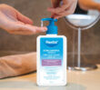 Hand pressing pump of Flexitol Acne Control Wash bottle with liquid dispensing into palm at a sink